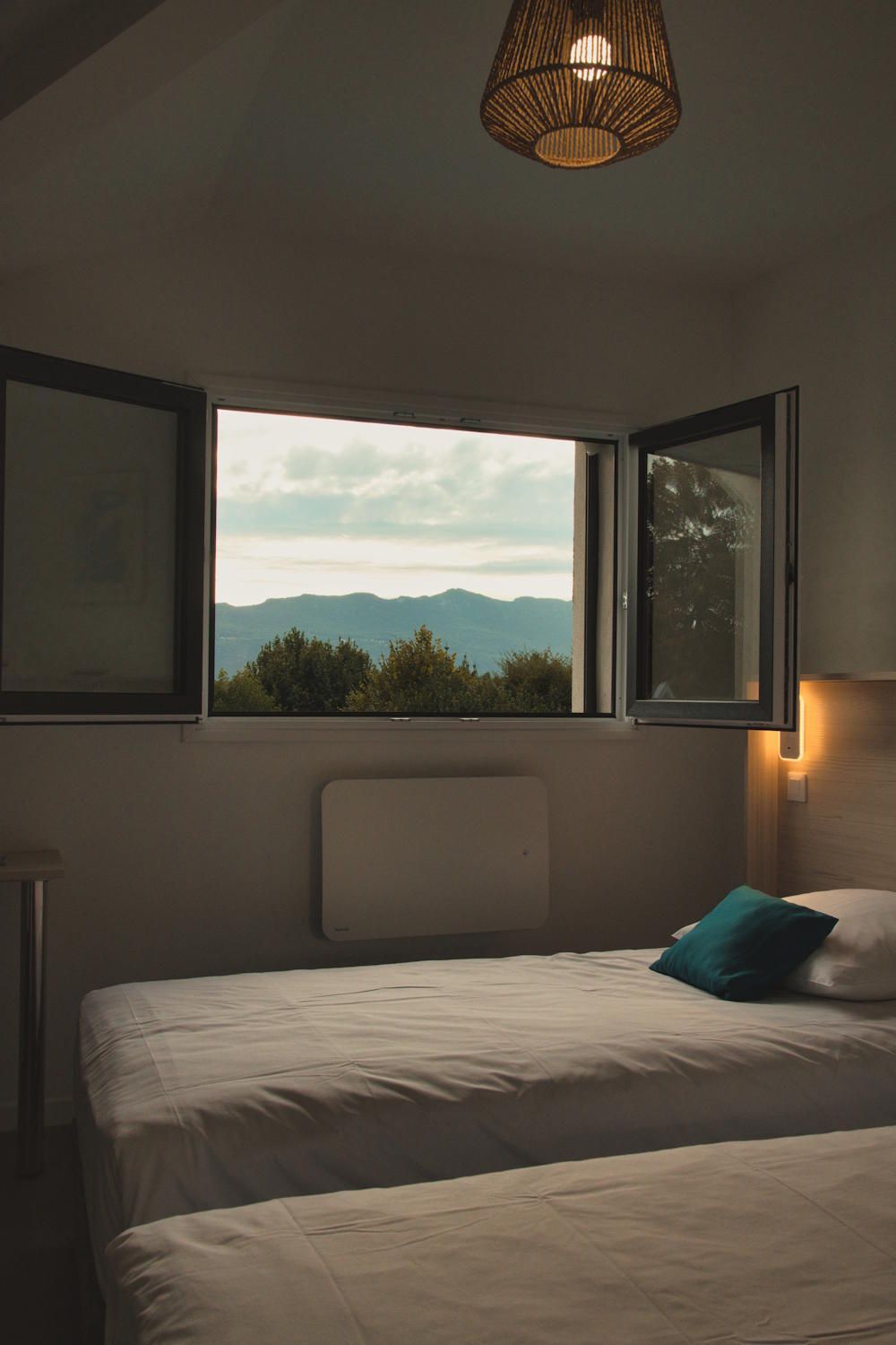 Une chambre à coucher avec un lit, une fenêtre donnant sur les montagnes et un luminaire suspendu.