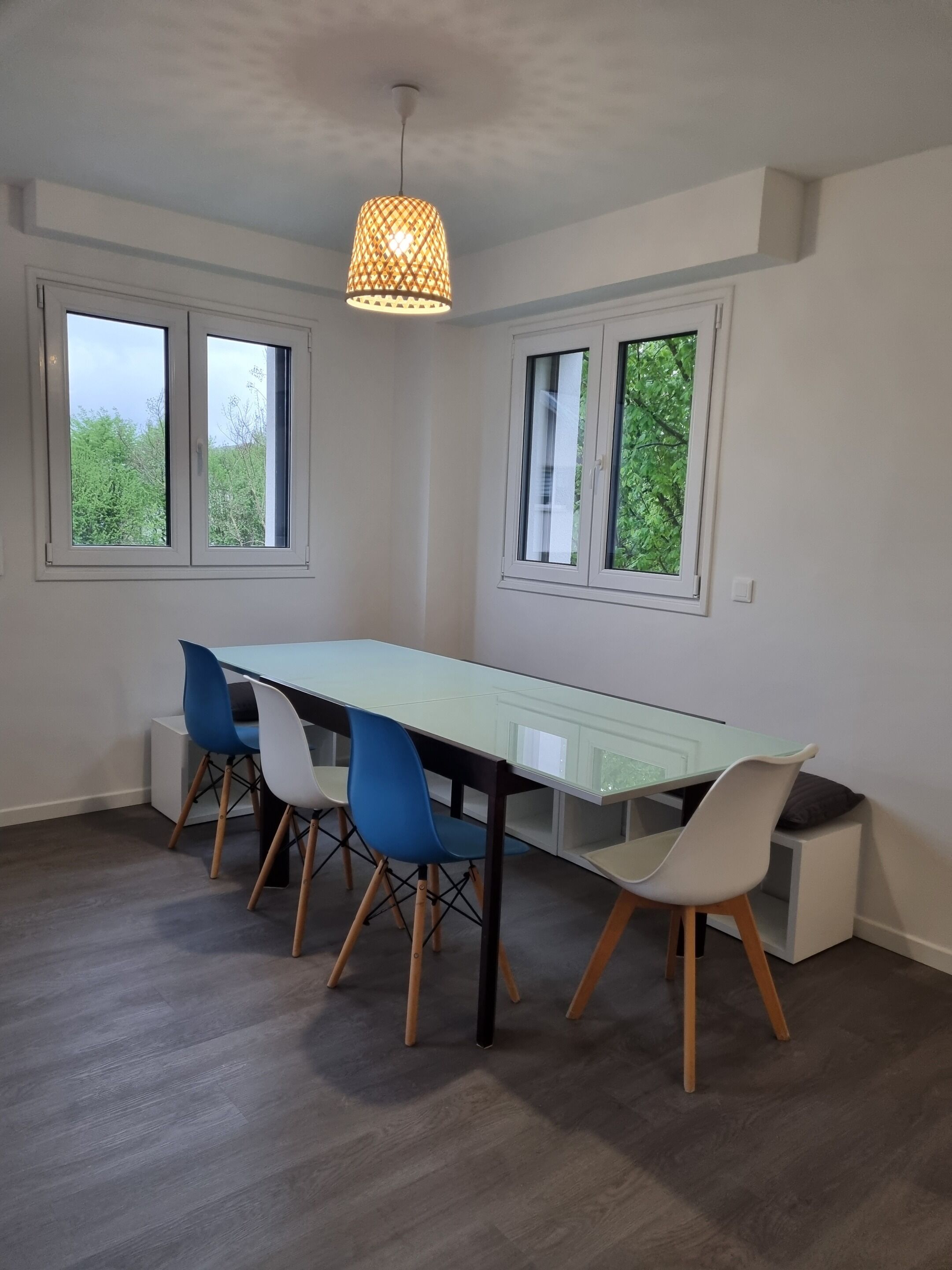 Un espace repas comprenant une longue table, quatre chaises et un luminaire suspendu.