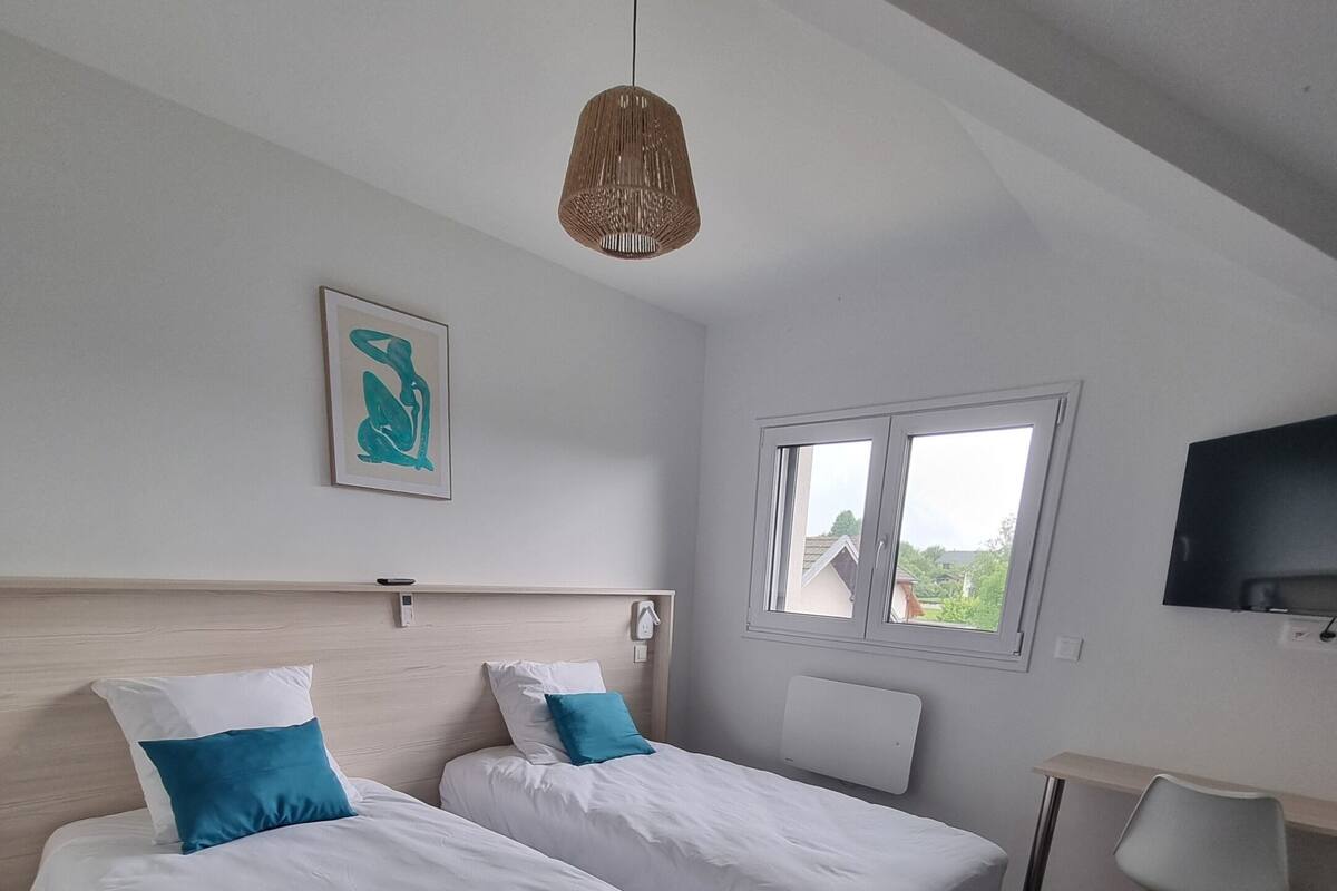Ein Zimmer mit zwei Betten, einem Schreibtisch, einem Fernseher und einem Fenster.