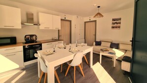 A modern kitchen with white cabinets, a dining table with chairs, a sofa, and a small TV. - Le Combo (Aix-les-Bains)