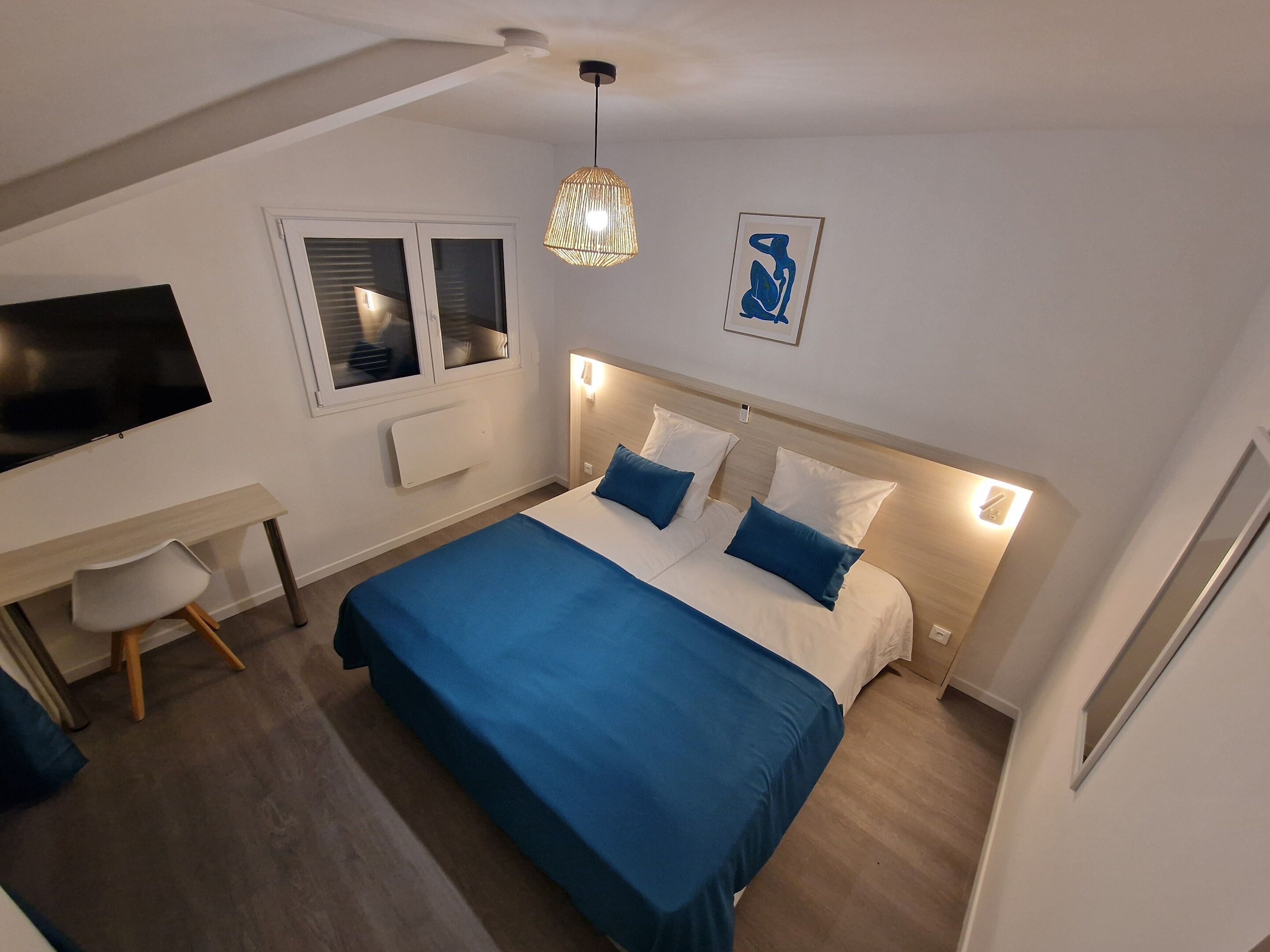 Un dormitorio con cama, lámparas de noche, un escritorio, una silla, un televisor y una ventana.