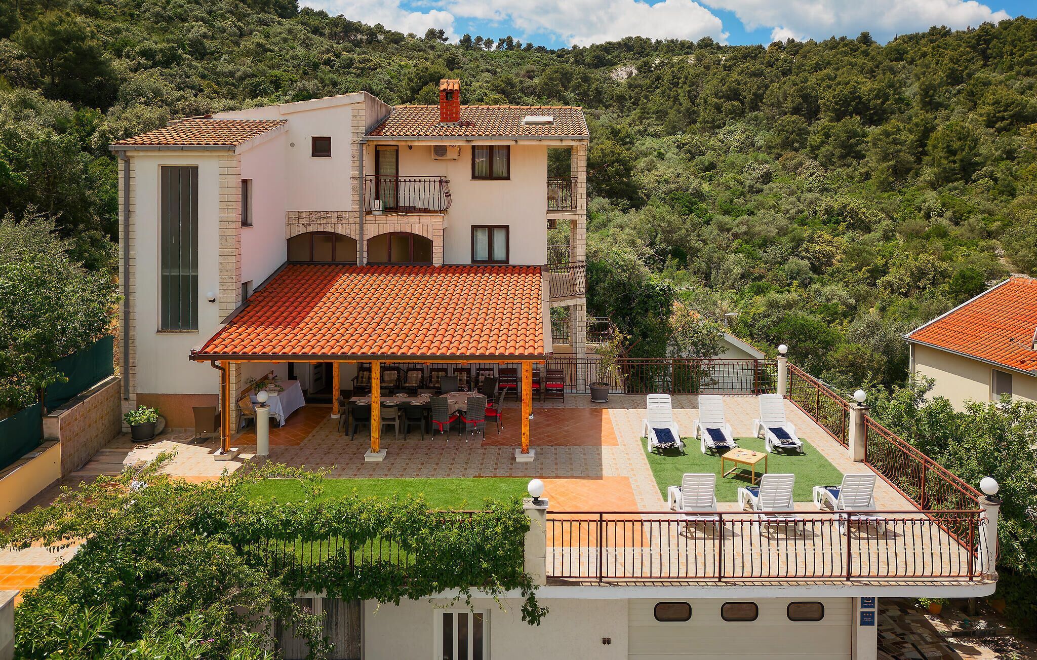 A two-story villa with a tiled roof, a covered patio with outdoor seating, and a pool area with lounge chairs.
