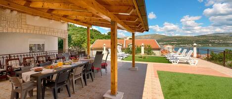 An outdoor dining area with a wooden pergola, a table set for a meal, and a view of a lake and hills in the background.