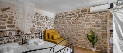 A bedroom with a bed, a yellow armchair, a potted plant, and a stone wall.