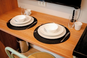 Una mesa de madera para comer con dos juegos de platos blancos, individuales negros y cubiertos.