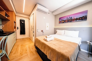 A hotel room with a bed, a painting, a kitchenette, and a door.