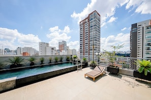 Piscina en la azotea con sillas de descanso, plantas en macetas y vistas panorámicas de la ciudad.