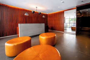 A modern interior with wooden panel walls, a reception desk, and three orange ottomans.