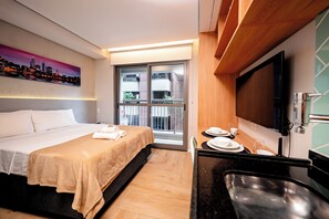 A hotel room with a bed, a dining table with plates and glasses, a TV, and a window with a cityscape view.