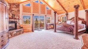 A spacious bedroom with a large bed, a stone fireplace, and a view of the outdoors.