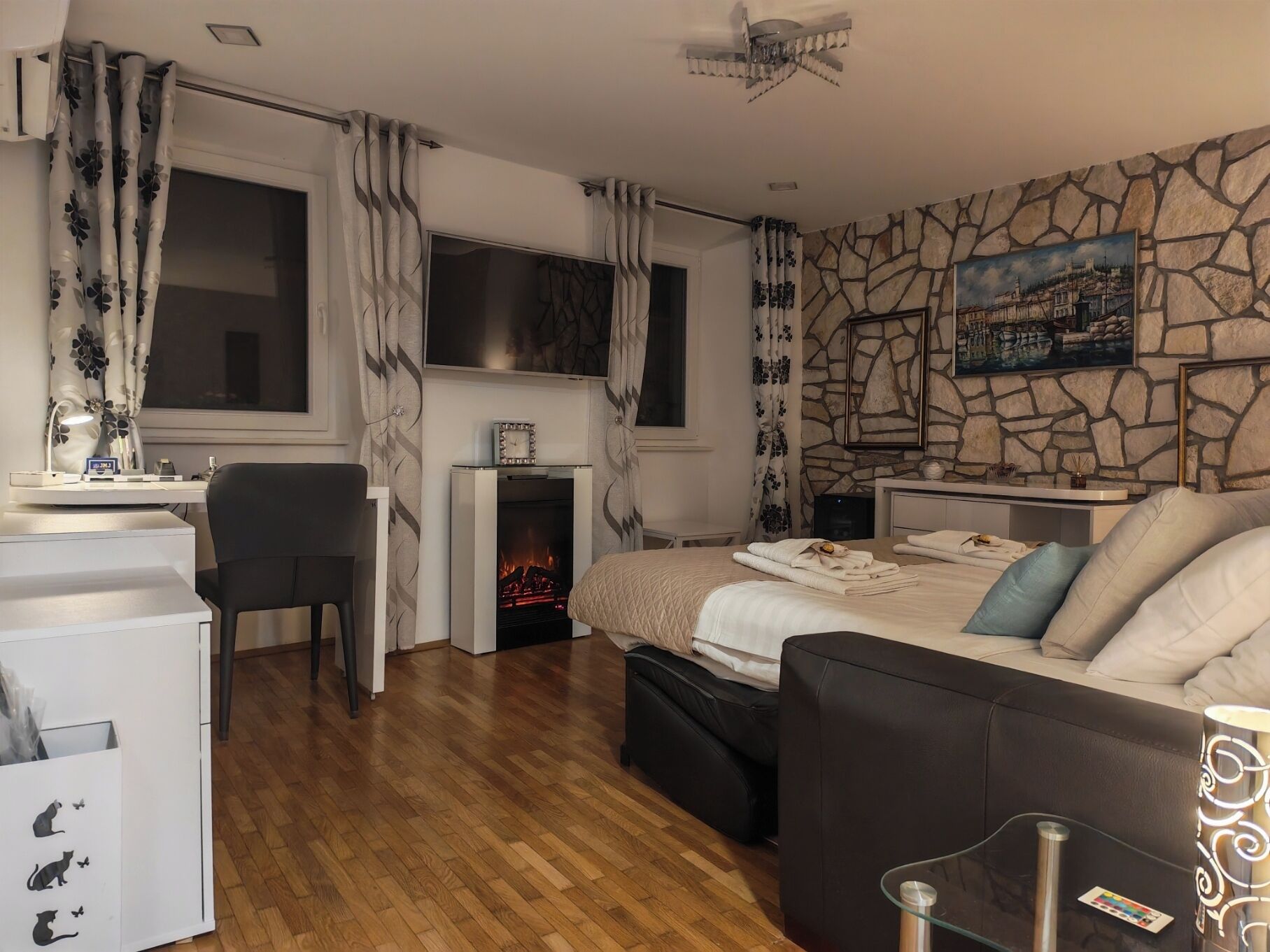 Un dormitorio moderno con chimenea, una cama con almohadas, un escritorio con silla y una pared de piedra con un cuadro.