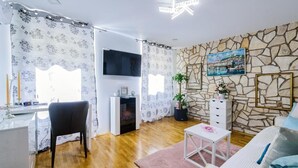 Ett vardagsrum med en vägg av sten, en öppen spis, en tv och en mysig sittgrupp.