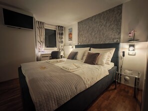 A modern hotel room with a large bed, bedside tables, a desk, and a window with curtains.