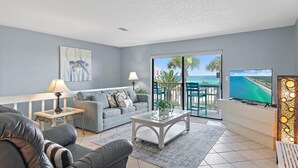 A modern living room with a grey sofa, a glass coffee table, and a TV on a white stand. - Gulf Winds East #10- The Turtles Nest (Miramar Beach)