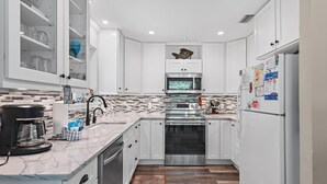 A modern kitchen with white cabinets, a stainless steel oven, a microwave, and a refrigerator. - Gulf Winds East #34 (Miramar Beach)