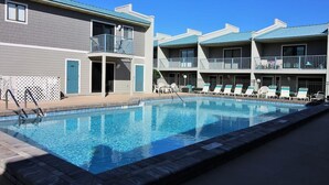 A poolside area with a swimming pool, lounge chairs, and a building with balconies. - Gulf Winds East #34 (Miramar Beach)