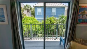 A room with a sliding glass door leading to a balcony with a view of a blue house and greenery. - Gulf Winds East #34 (Miramar Beach)