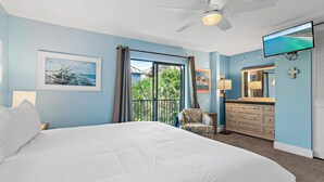 A bedroom with a large bed, a ceiling fan, a TV, a chair, a dresser, and a window with curtains. - Gulf Winds East #34 (Miramar Beach)