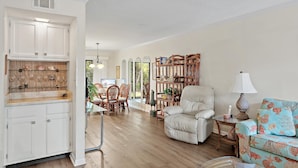 A spacious living room with a sofa, a dining area with chairs, and a kitchen with white cabinets and a wooden countertop. - Gulf Winds East #36 (Miramar Beach)