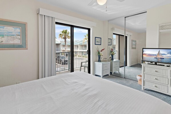 A hotel room with a large bed, a dresser, a television, and a balcony with a view of a resort.
