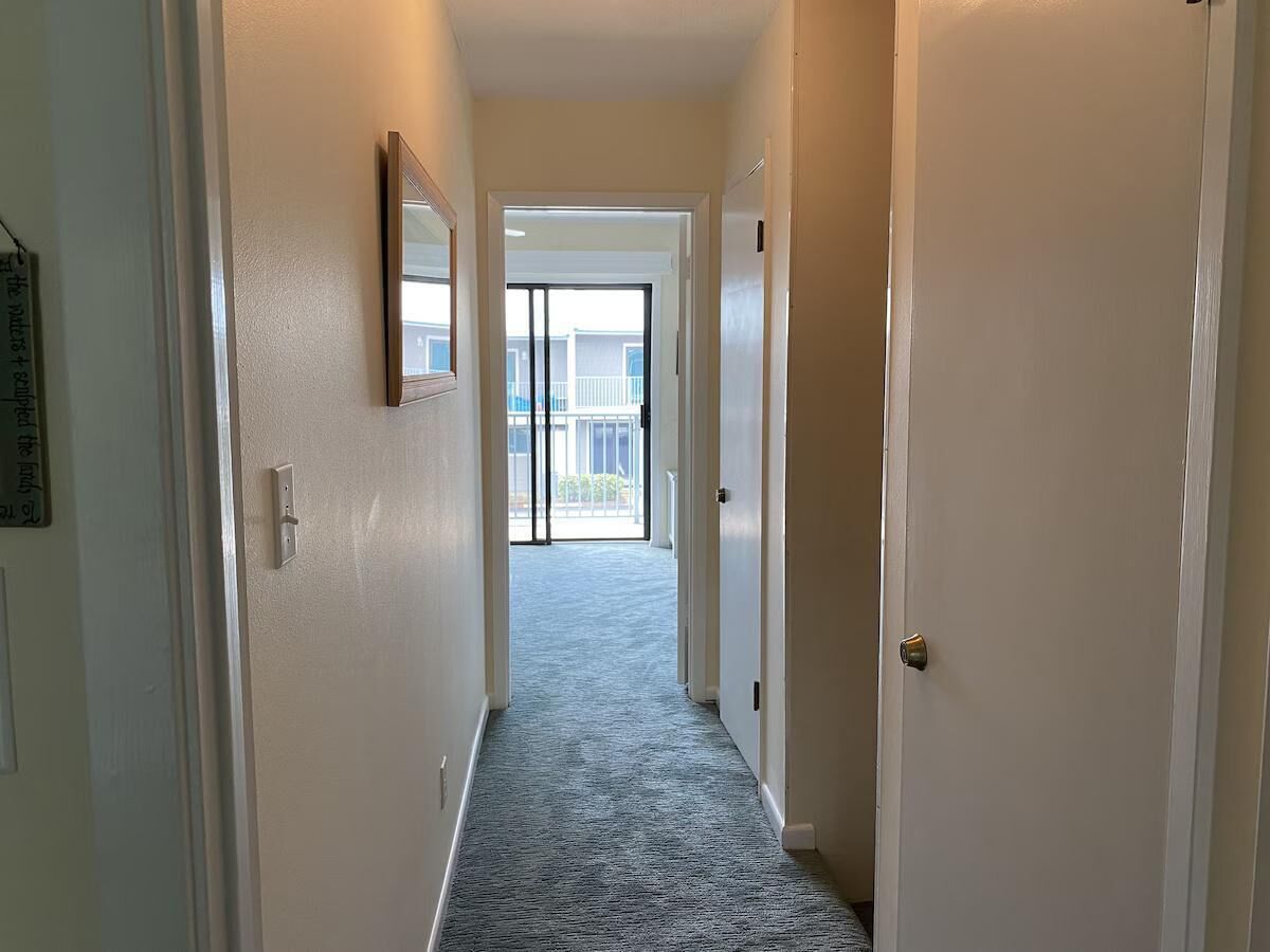 A hallway with a carpeted floor, a door on the right, and a glass door at the end leading outside.