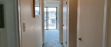 A hallway with a carpeted floor, a door on the right, and a glass door at the end leading outside.