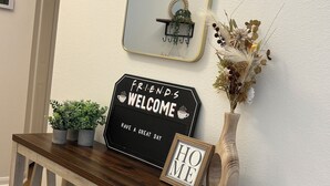 A wooden console table with a mirror, a welcome sign, and a small potted plant. - Charming 3-bedroom house  in delightful Katy! Perfect for family groups! (Katy)