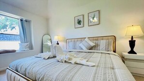 A neatly made bed with patterned bedding, a bedside table with a lamp, and a window with curtains. - Charming 3-bedroom house  in delightful Katy! Perfect for family groups! (Katy)