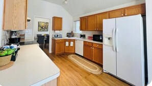 A kitchen with wooden cabinets, a white refrigerator, and a dining area with a table and chairs. - Charming 3-bedroom house  in delightful Katy! Perfect for family groups! (Katy)