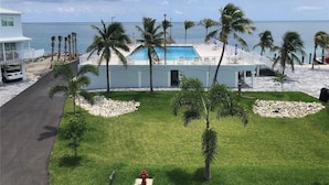 Zona de piscina con palmeras, un edificio y vista al océano.