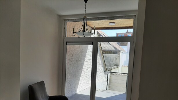 A room with a large sliding glass door leading to a balcony, a black chair, and a ceiling light fixture.