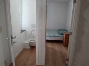 A small, clean room with a toilet, a bed with a green pillow, and a wooden nightstand. - Spacious apartment sleeps 9 Central (Oostende)