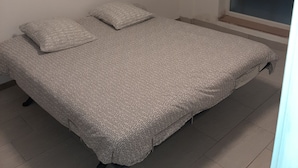 A small, single-bed room with a patterned bedspread, a window with a view, and a plain white wall.