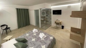 A modern hotel room with a bed, a desk, a chair, a shower area, and a TV. - Secretplace Palermo (Palermo)
