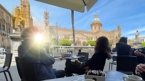 An outdoor cafe with tables and chairs, a statue in the foreground, and historic buildings in the background. - Secretplace Palermo (Palermo)