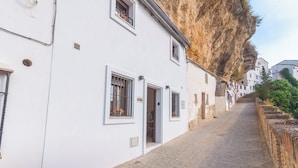 A narrow cobblestone street flanked by white buildings with barred windows and a steep cliff. - Un Rinconcito en Setenil Setenil de las Bodegas by Ruralidays (Cádiz)