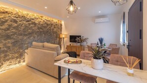 A modern living room with a stone accent wall, a sofa, a dining table with chairs, and a TV. - Un Rinconcito en Setenil Setenil de las Bodegas by Ruralidays (Cádiz)