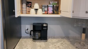 A kitchen with a coffee maker, a cabinet with bowls, cups, and coffee pods. - Fisherman's Paradise w/ Waterfront and 2 KING suites. Bring your boat! 40' dock (Homosassa)