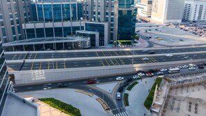 Vue aérienne d’un quartier urbain moderne, avec un parking à plusieurs niveaux, une route sinueuse et des immeubles de grande hauteur.
