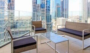 Een balkon met rieten meubels, een glazen tafel en uitzicht op de stad.