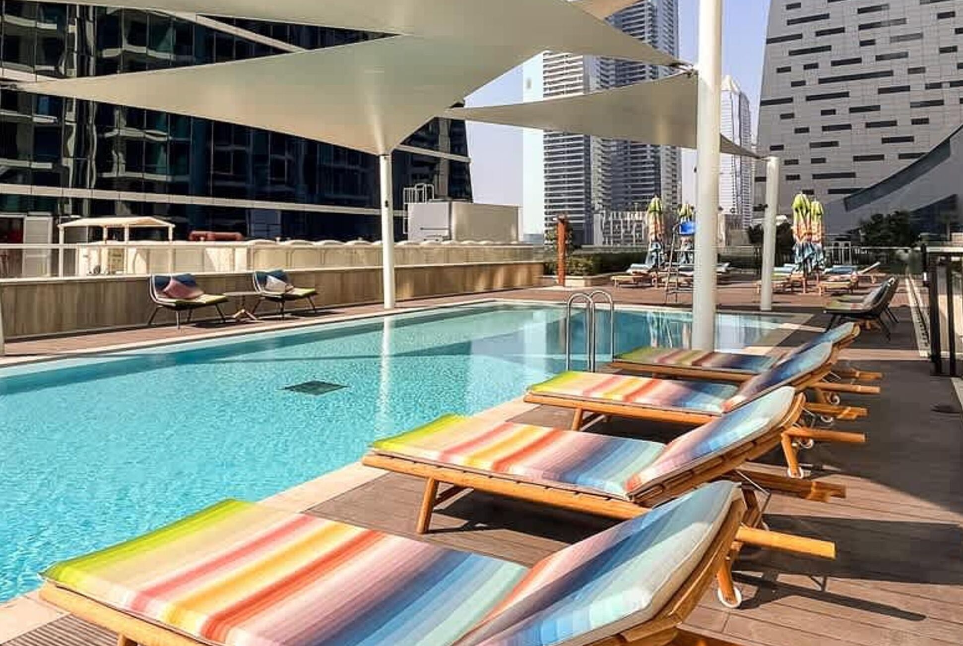 Piscina en la azotea con sillones de descanso y vistas a edificios modernos.