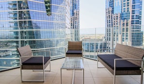 A high-rise balcony with modern wicker furniture, glass railings, and a city view.