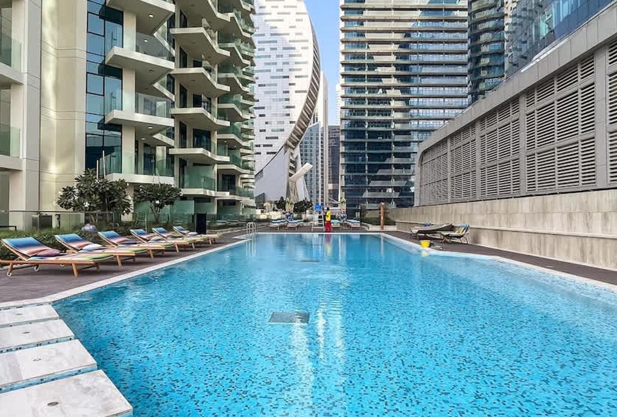 Una piscina con lettini, circondata da edifici alti.