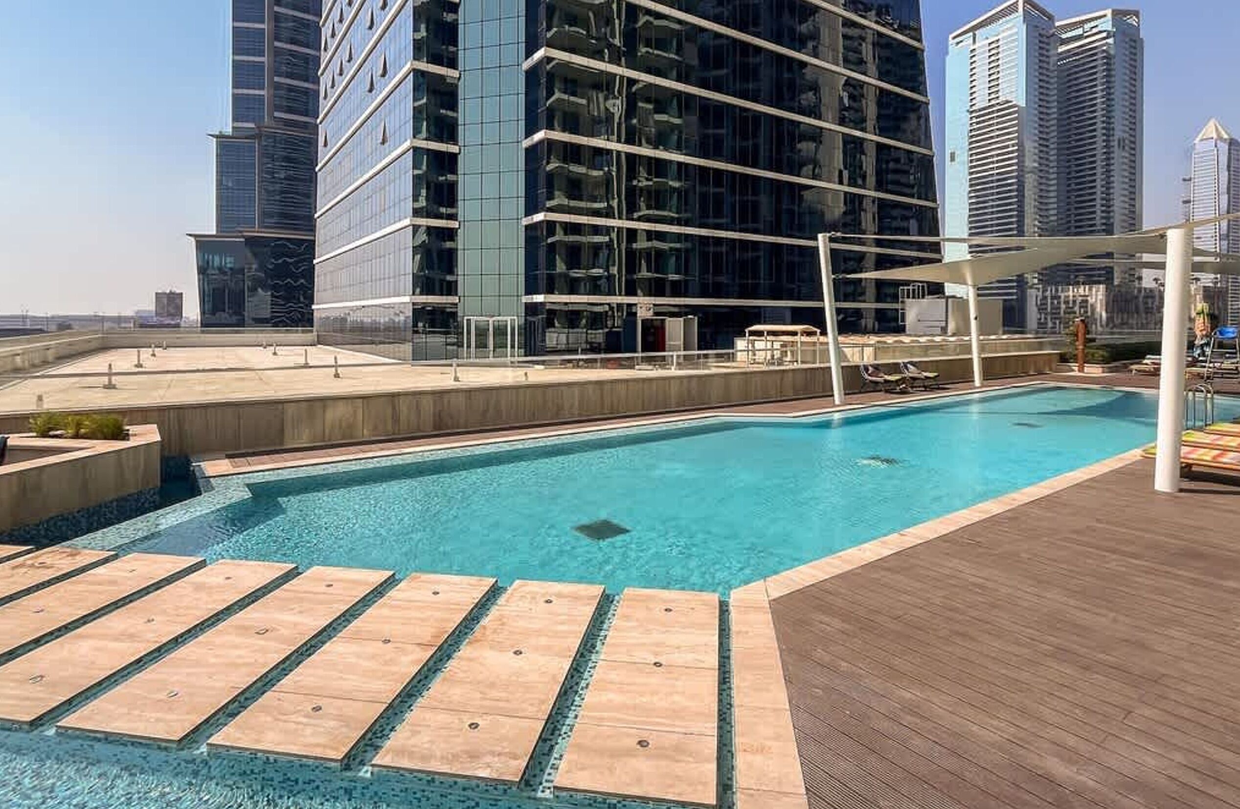 Una piscina en la azotea con un muelle de madera, rodeada de edificios altos.