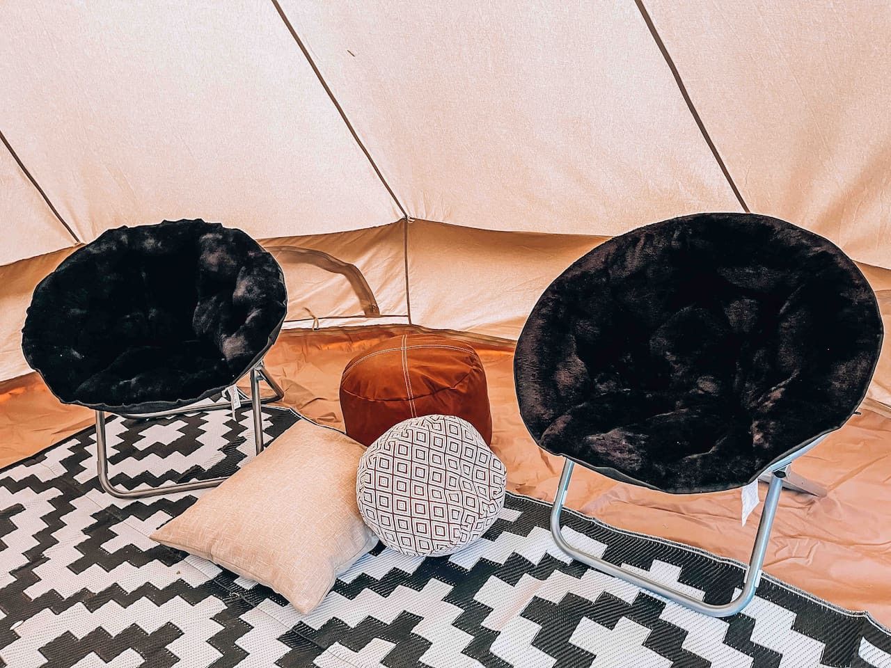 A tent interior with two black velvet chairs, a patterned cushion, and a brown ottoman.