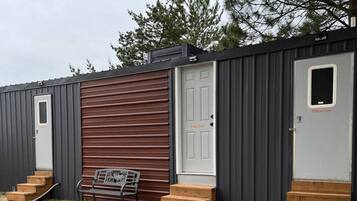A row of mobile homes with external steps leading to the doors, a bench, and a grassy area.