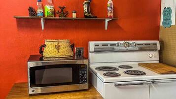 A kitchen with a white stove, a microwave on a wooden table, and shelves with kitchen items against a red wall.