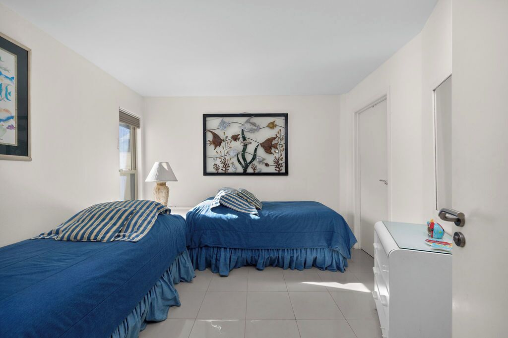 Un dormitorio con dos camas, una ventana, una lámpara y una obra de arte enmarcada en la pared.