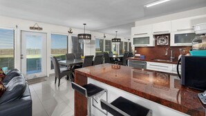 Una cocina moderna con encimeras de granito, electrodomésticos de acero inoxidable y un comedor con sofá de cuero negro y sillas.