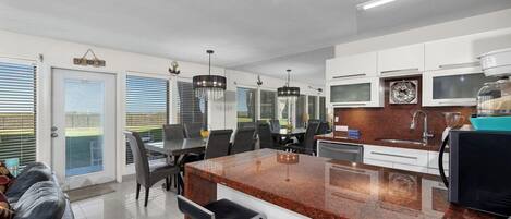 A modern kitchen with granite countertops, stainless steel appliances, and a dining area with a black leather couch and dining chairs.